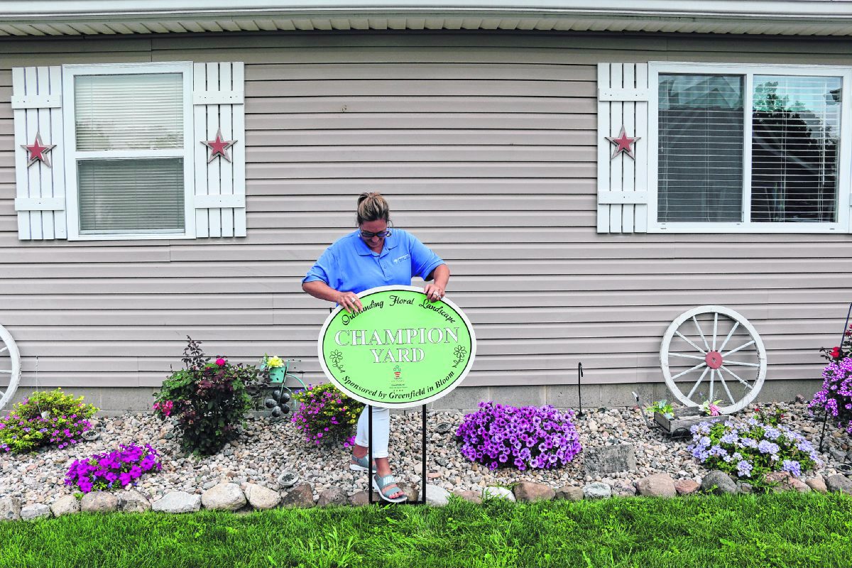 Bobbi Anderson, director of Greenfield in Bloom, plants a Champion Yard sign in front of a home to recognize its vibrant floral display. Submitted